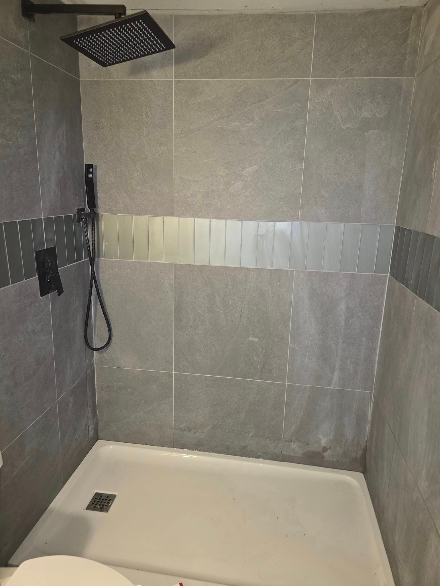 Une douche avec une pomme de douche noire et un receveur de douche blanc.