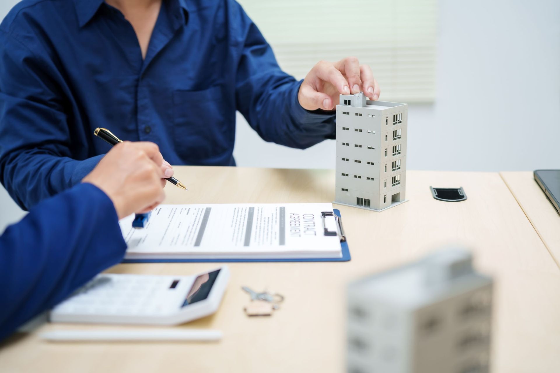 A Man Is Sitting At A Table With A Clipboard And A Model House