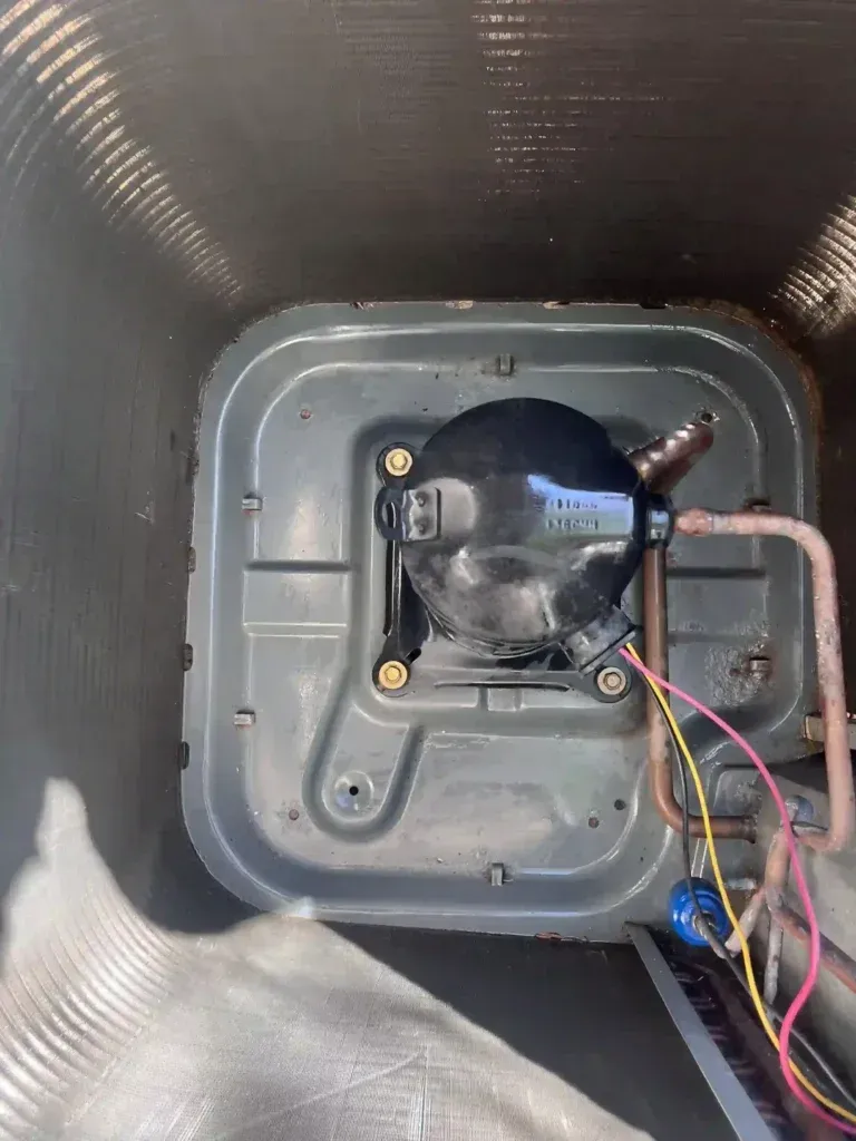 AC compressor inside unit, with copper tubing and wiring.