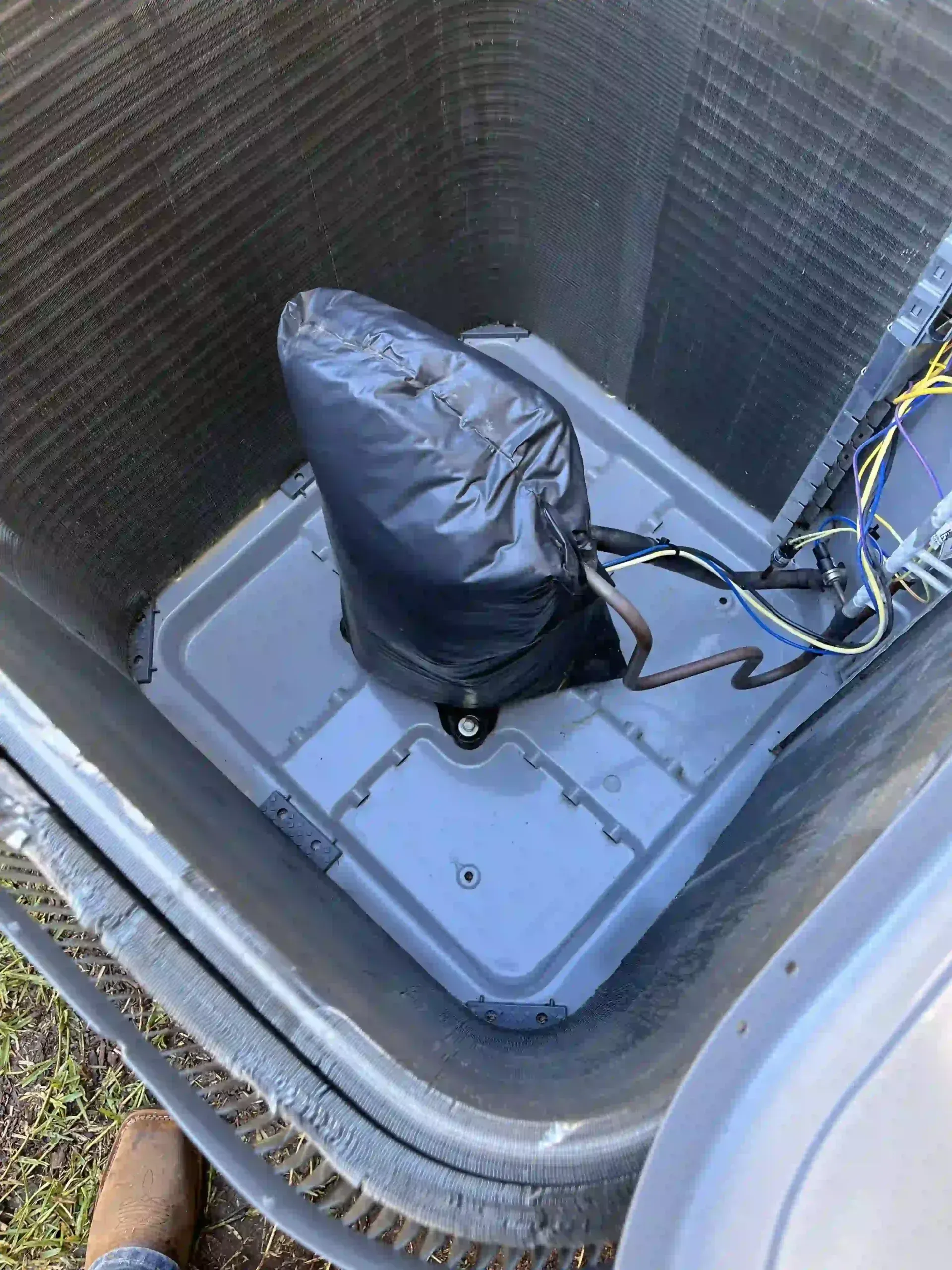 Air conditioning unit with a black plastic bag over a component, likely for weather protection. Gray and dark colors dominate.