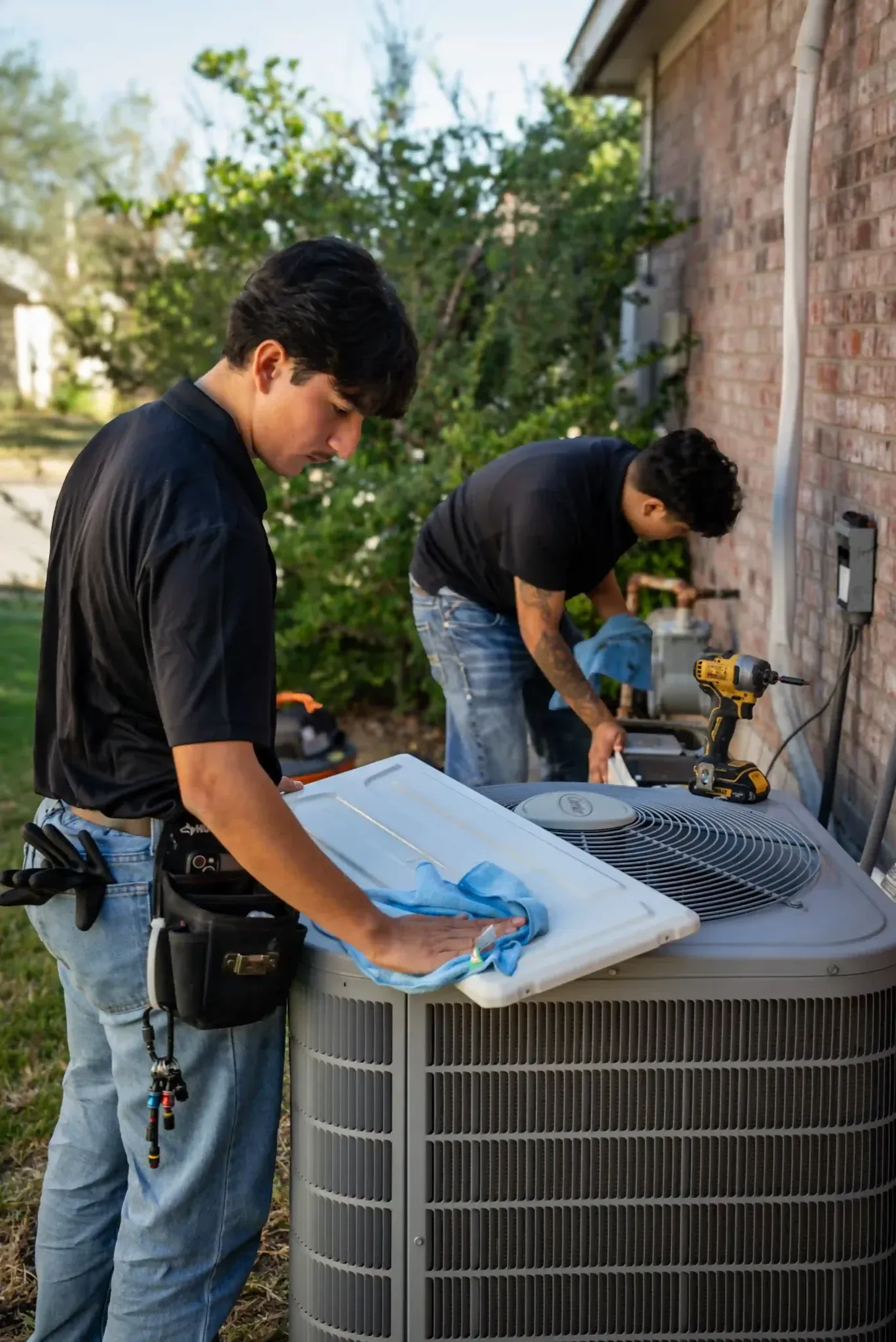 Two technicians cleaning and servicing an AC unit outdoors.