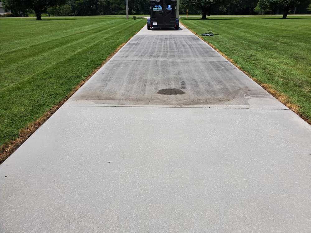 A forklift is driving down a concrete driveway next to a lush green field.