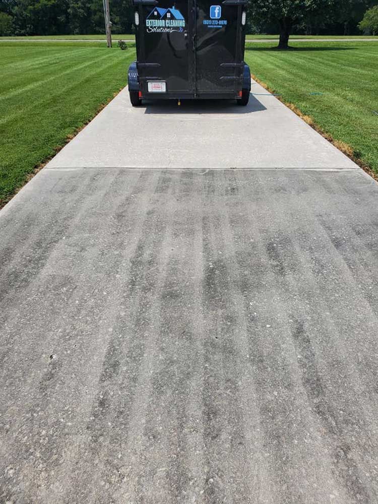 A black trailer is parked on the side of a concrete driveway.