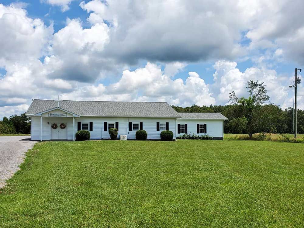 A white house is sitting on top of a lush green field.