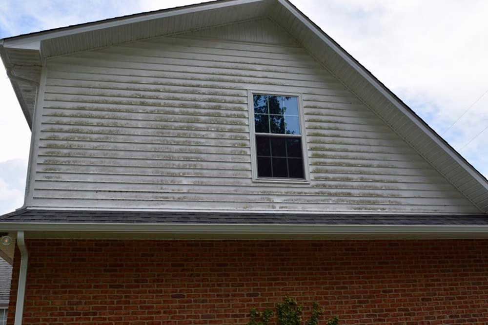 The side of a brick house with a white siding and a window.