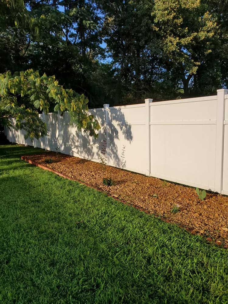 A white fence surrounds a lush green lawn in a backyard.