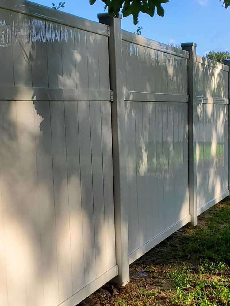 A white vinyl fence is sitting on top of a lush green field.