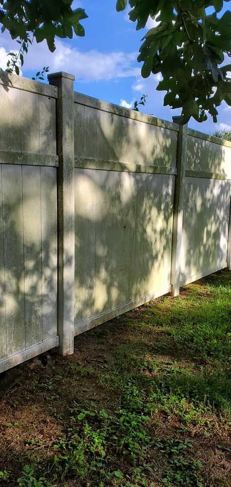 A white fence is surrounded by grass and trees in a yard.