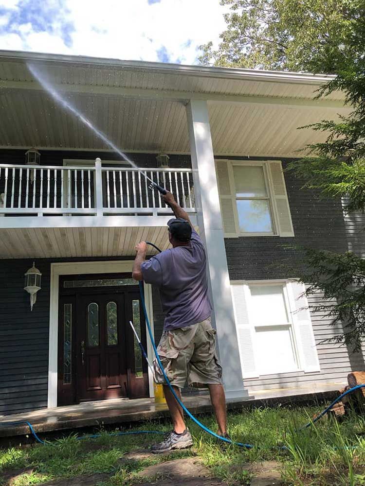 A man is cleaning the roof of a house with a pressure washer.