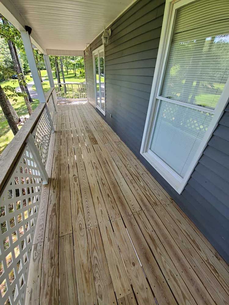 A long wooden porch with a white railing and windows on a house.