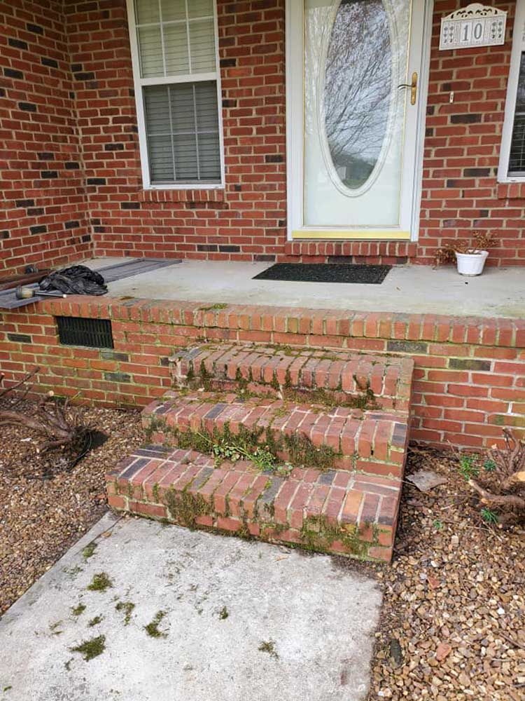 A brick porch with moss growing on the steps and a white door.