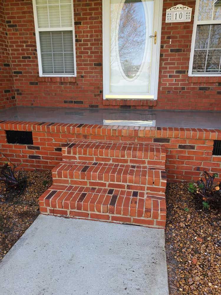 A brick porch with stairs leading up to the front door of a house.