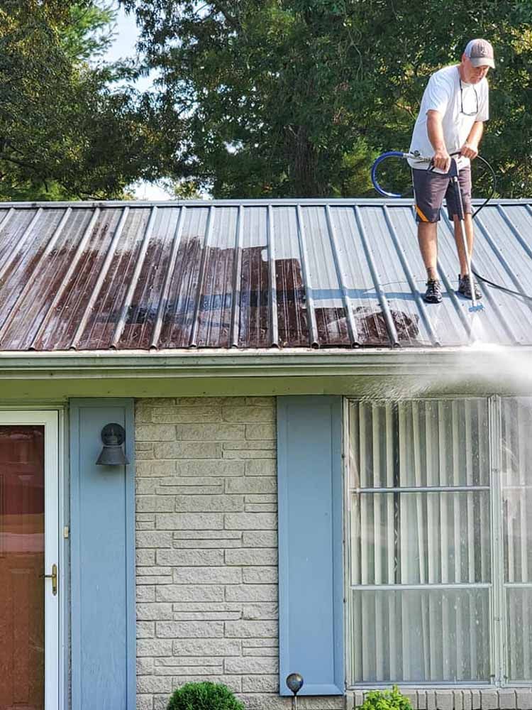 A man is cleaning the roof of a house with a high pressure washer.