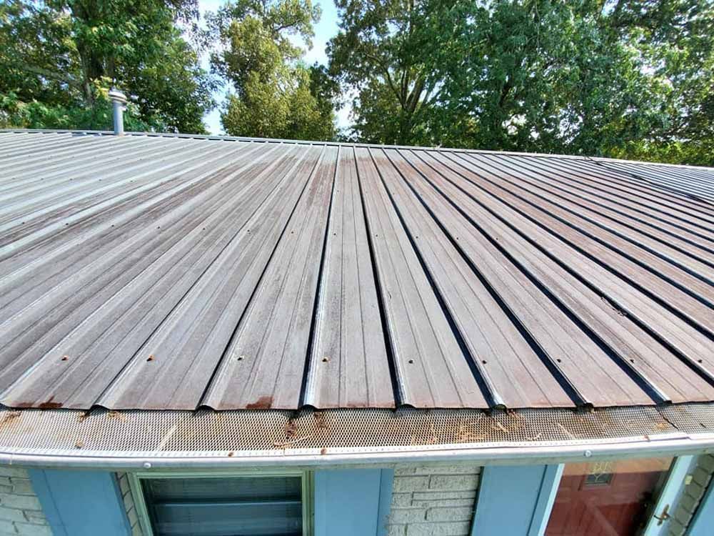 A close up of a metal roof on a house with trees in the background.