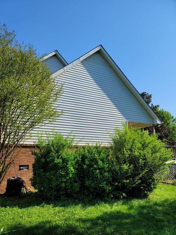 A white house with a blue sky in the background is surrounded by trees and bushes.