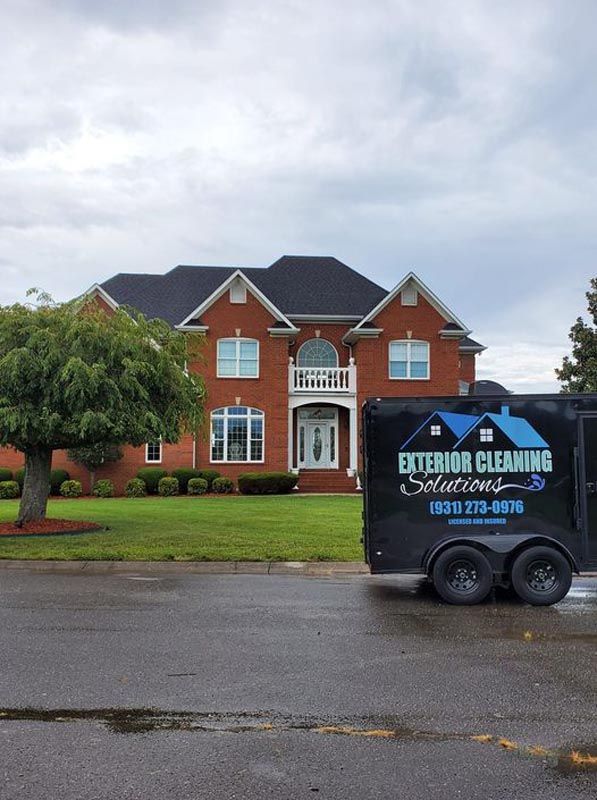 A trailer for exterior cleaning solutions is parked in front of a large brick house.