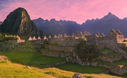 There is a castle in the middle of a field with mountains in the background.