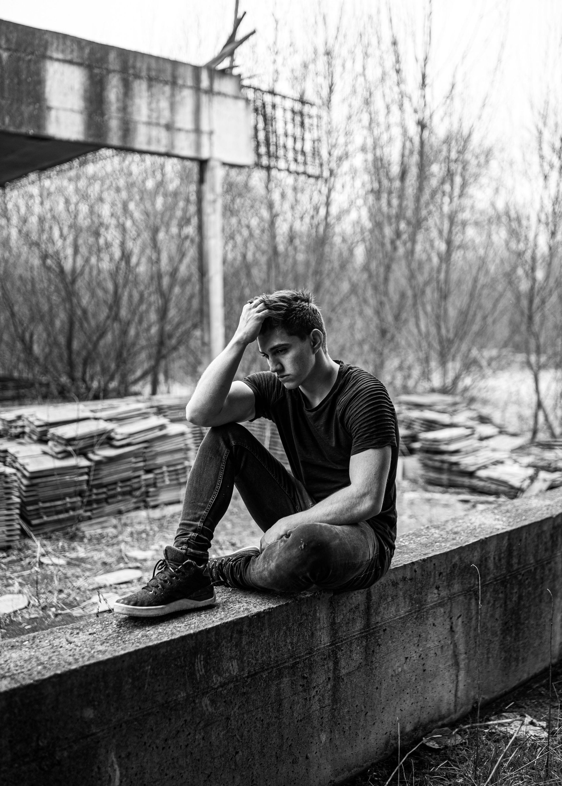 A black and white photo of a man sitting on a wall.