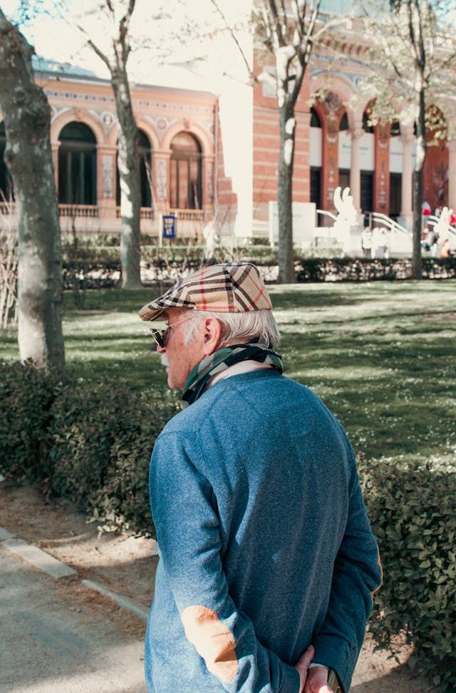 A man wearing a hat and scarf is standing in a park.