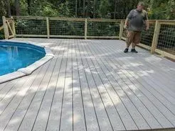 Man on a gray deck next to a pool, surrounded by a fence in an outdoor setting.