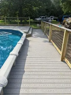 Decking with a cable railing leading to a pool with light gray composite decking.
