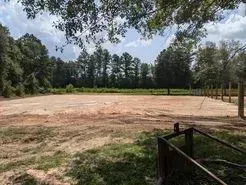Cleared, dirt field surrounded by trees with a wooden fence in the foreground.