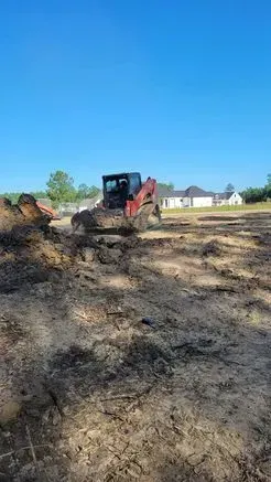 A skid steer is operating on a muddy construction site under a clear blue sky.