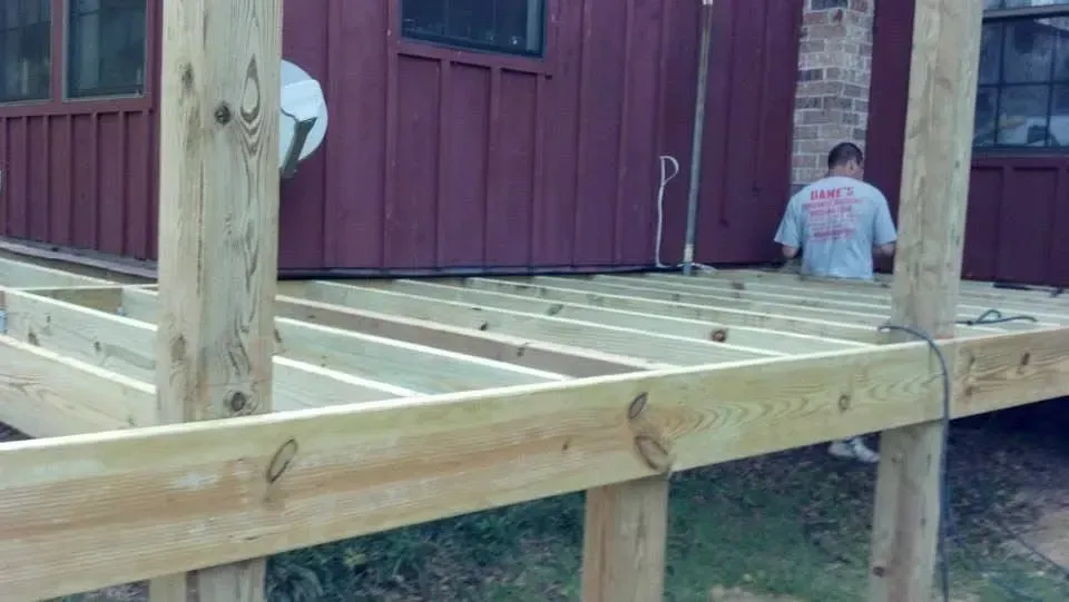Wooden deck construction with a person working near a red building.