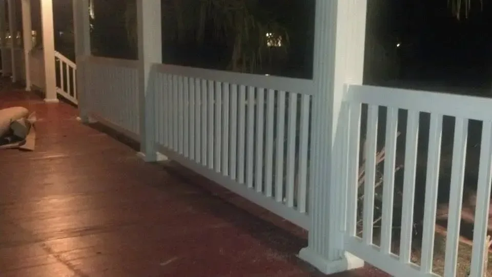 White porch railing and columns on a wooden floor at dusk.