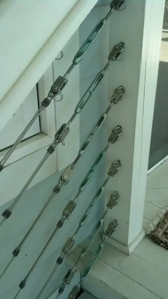 White wooden railing with angled metal cables and turnbuckles for support.