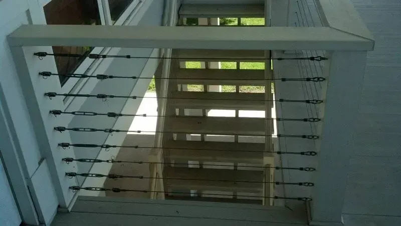Staircase with horizontal metal cable railing. White painted wood, looking down.