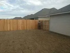 Wooden fence encloses a backyard with a person standing by a gate.