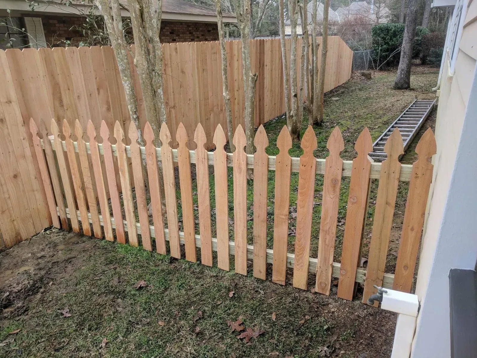 Wooden picket fence in a backyard, with a taller wooden fence in the background.