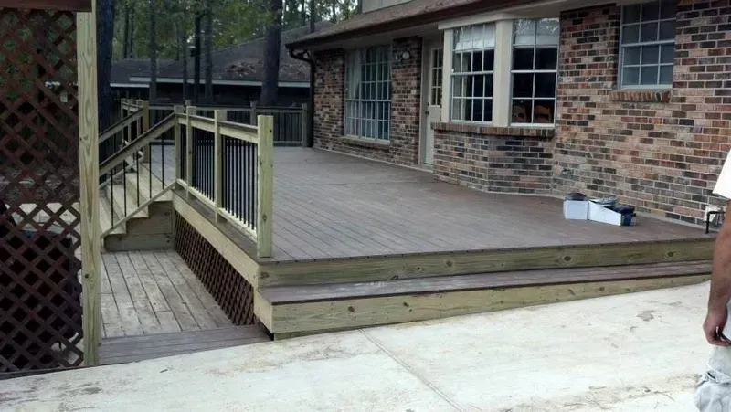 Exterior view of a wooden deck built adjacent to a brick house, featuring stairs and a lattice railing.
