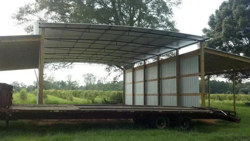 Trailer with a metal-roofed shelter, set in a grassy field with trees in the background.