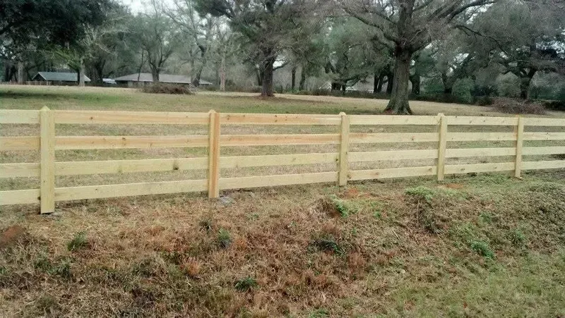 Wooden rail fence in a grassy field, trees in the background.
