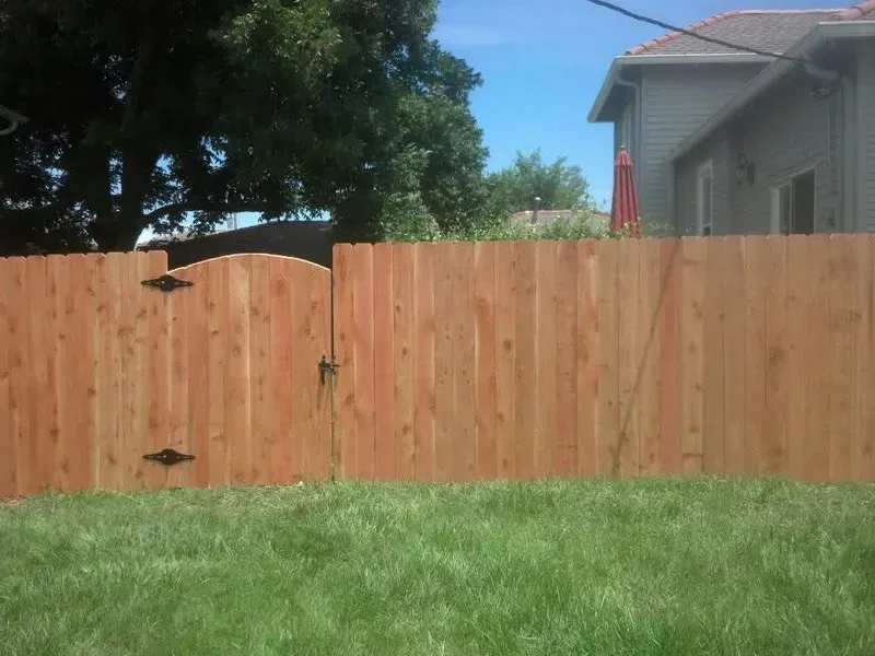 Wooden fence with gate in front of a green lawn and house, under a blue sky.