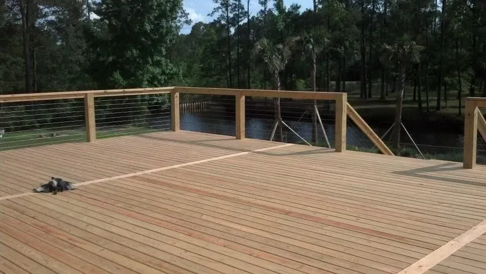 Wooden deck with a cable railing overlooking a body of water and trees. A small animal is on the deck.