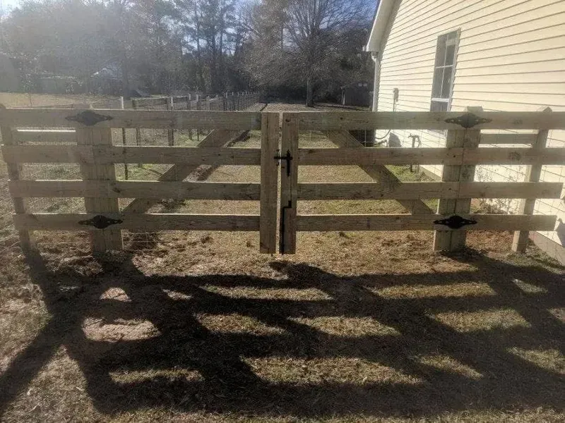 Wooden gate in front of a house, gate is open with black hinges and a latch.