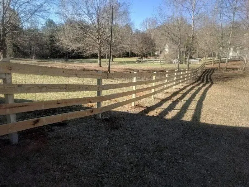 Wooden fence in a field, casting long shadows on a sunny day.