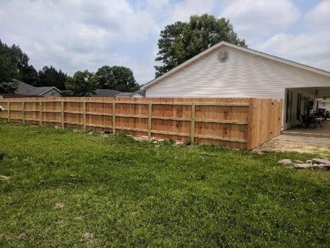 Wooden fence in a grassy backyard next to a house under a cloudy sky.