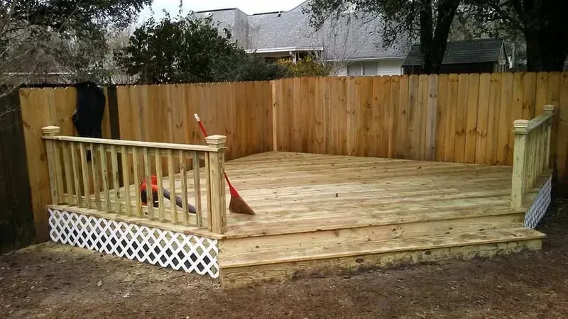 Wooden deck with lattice skirting, railing, and a wooden fence backdrop.