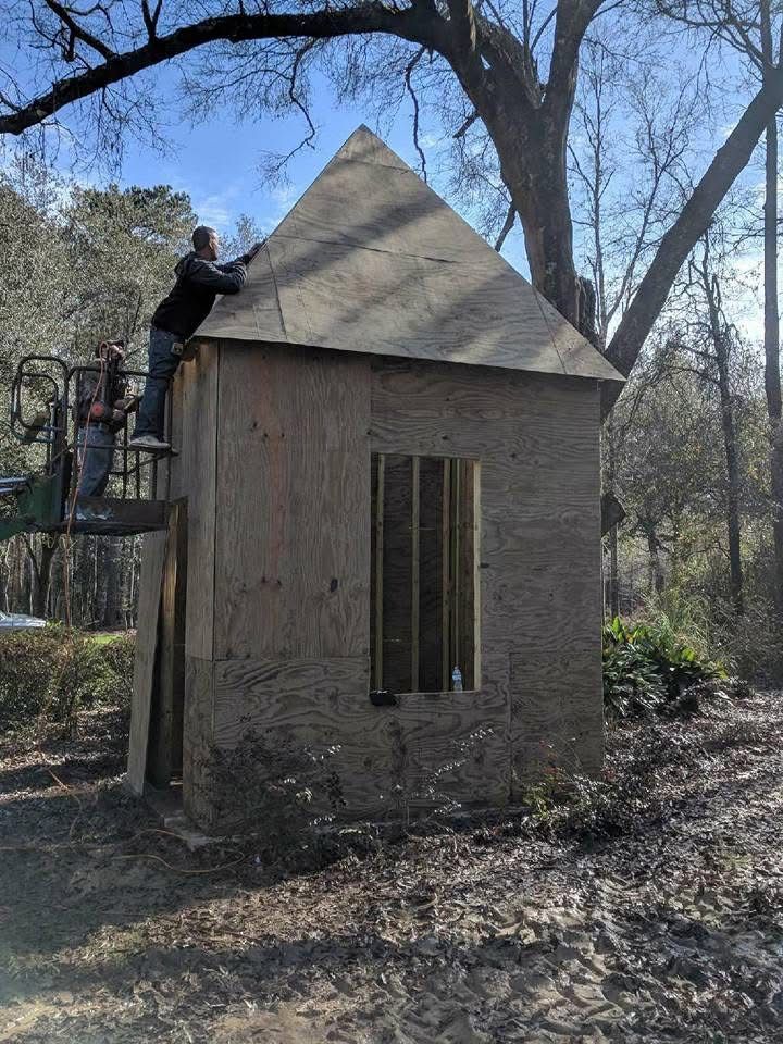 Two people on lift installing roof on small wooden structure outdoors.