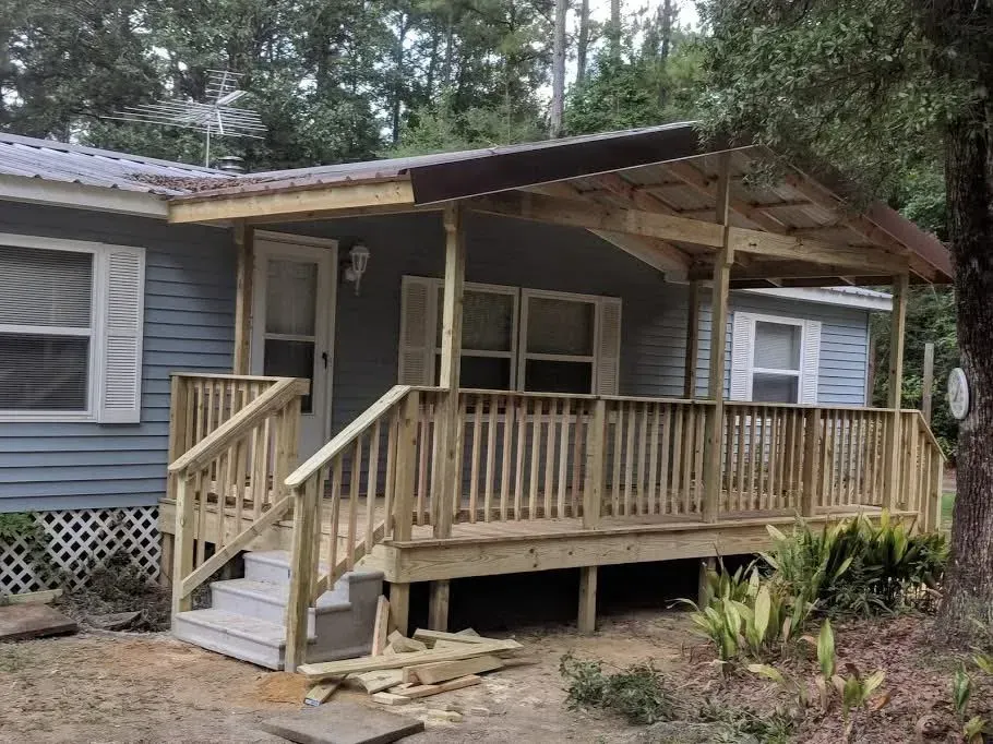 A house with a newly built wooden porch and ramp under a metal roof. Blue siding and white trim.