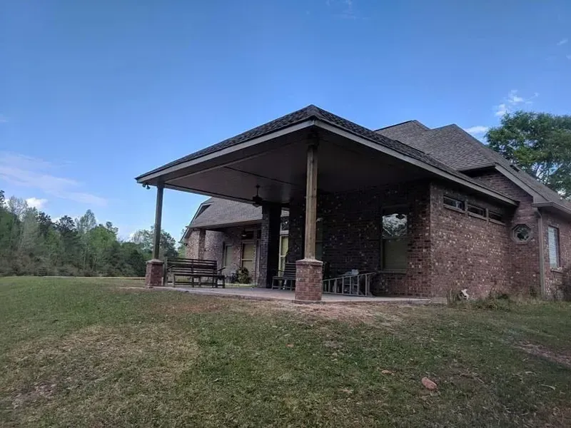 Brick house with large covered patio, dark roof, and blue sky background.