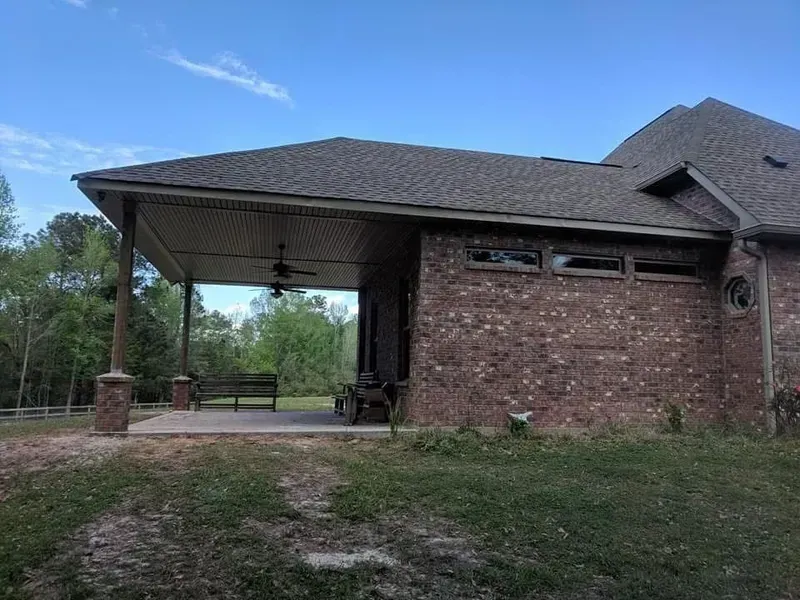 A brick house with a covered porch, brown roof, and green lawn.