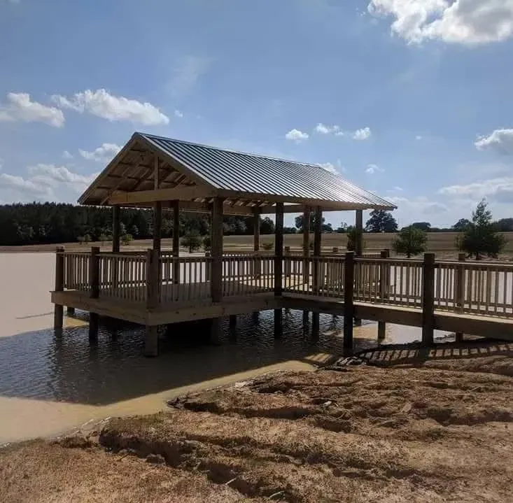 Wooden gazebo on a pier over a lake under a blue sky.