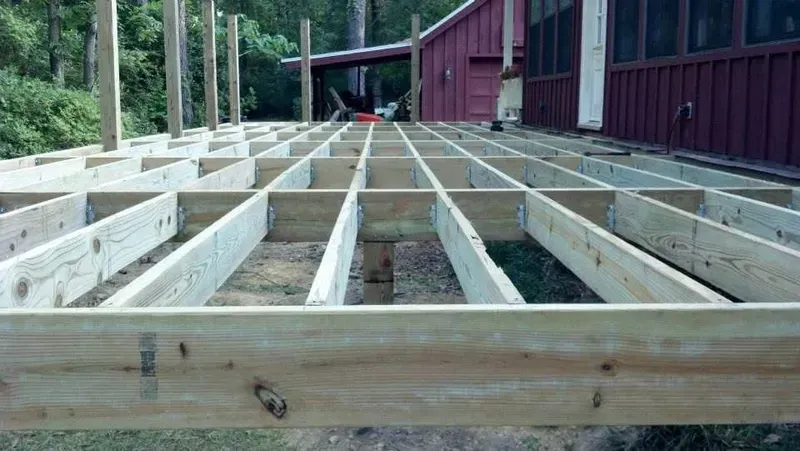 Wooden deck frame under construction next to a red building.