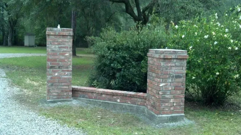 Brick pillars and low brick wall at a driveway entrance, surrounded by greenery.