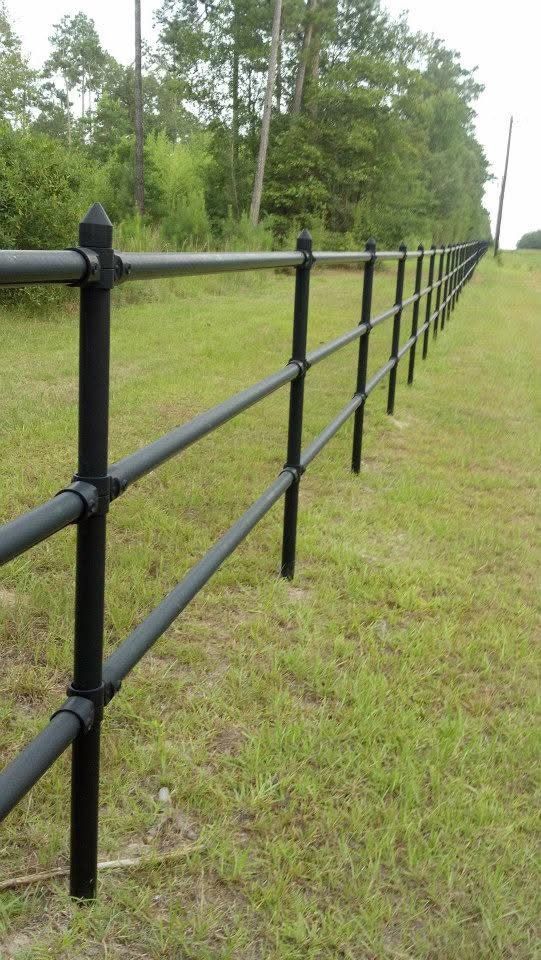 Black metal fence in a grassy field with trees in the background.